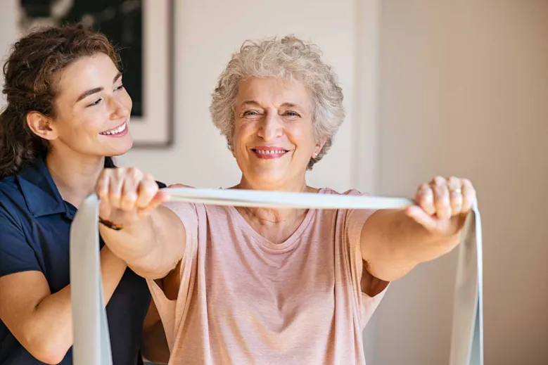 Smiling older woman stretching a resistance band with help from a younger woman