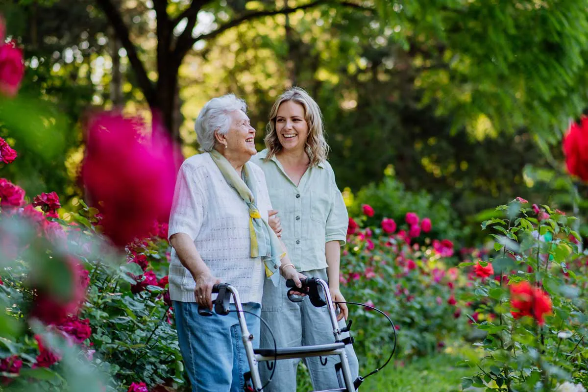 Older woman with a walker walking with a younger woman in a rose garden
