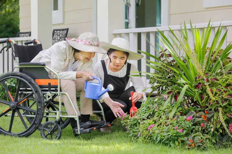 Older woman in a wheelchair watering plants with a younger woman