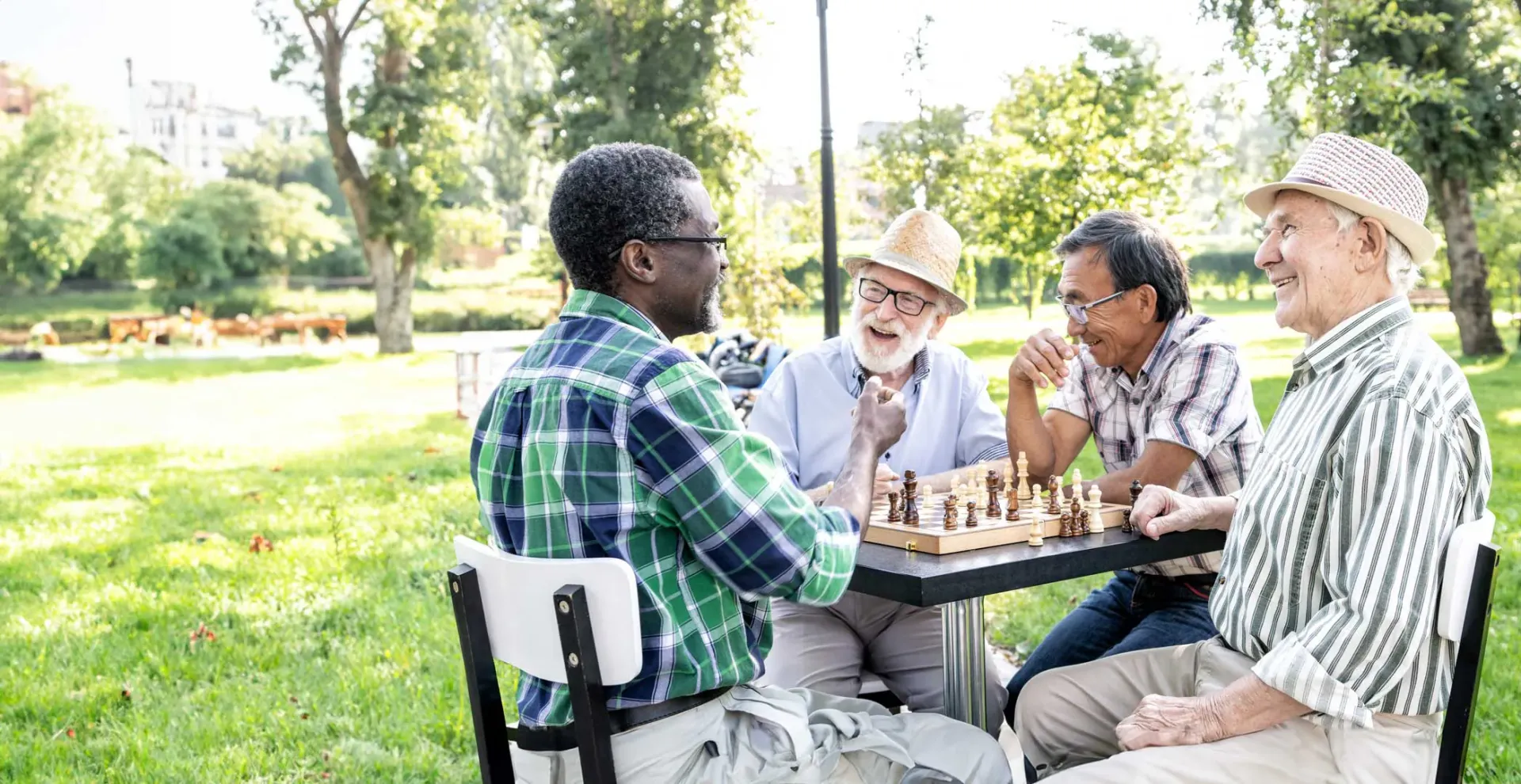 Four older men playing chess at a table in a park