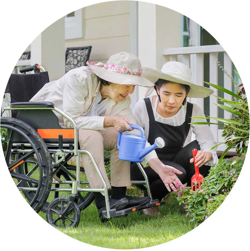 Older woman in a wheelchair watering plants with a younger woman